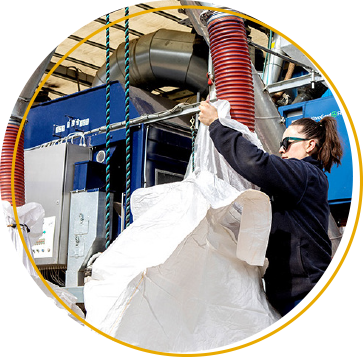 a mobile seed specialist holding a dumpy bag around a pipe that is used to pour treated seed into the bag